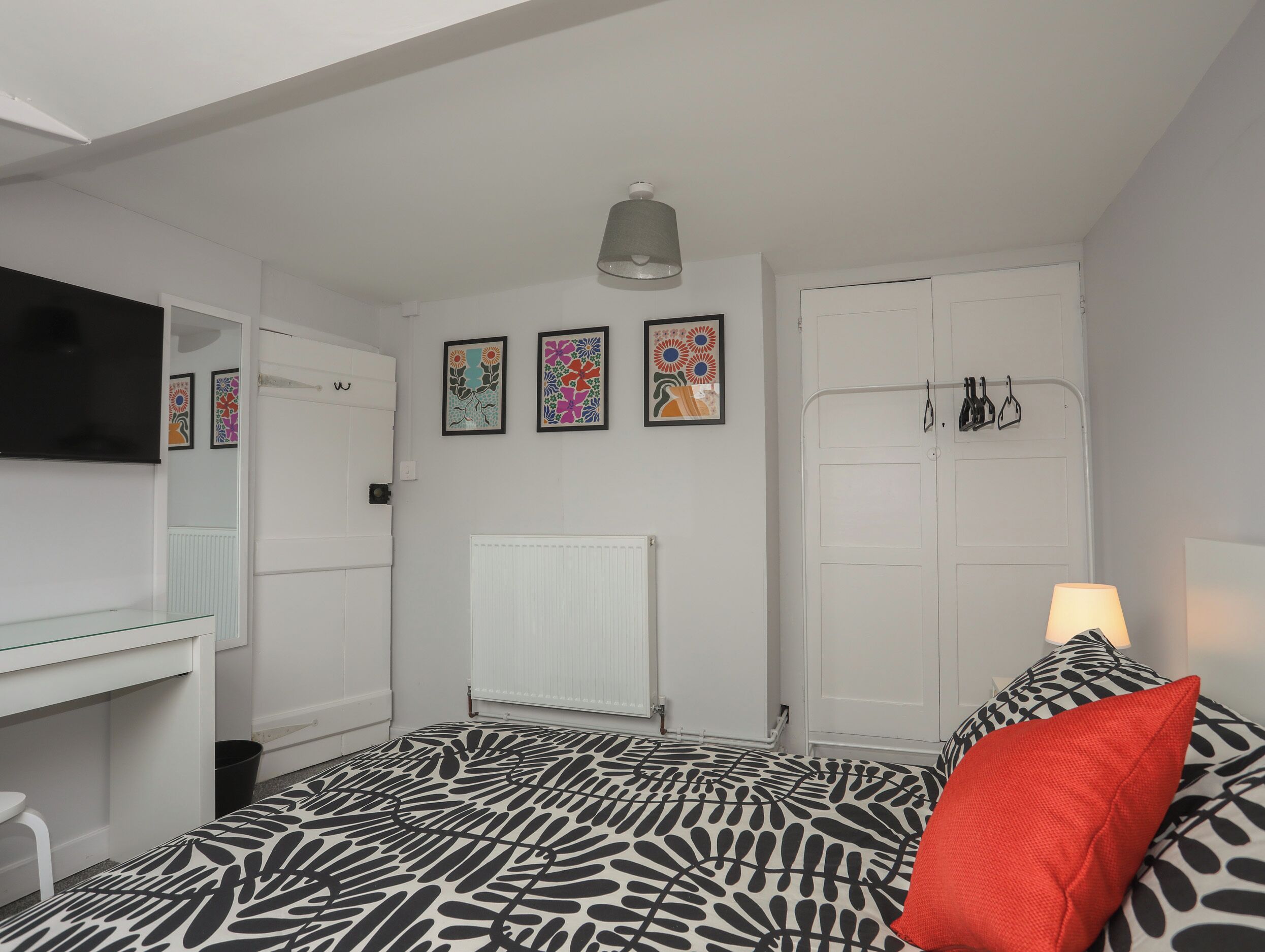 Un dormitorio con cama, escritorio, radiador y obras de arte en la pared.