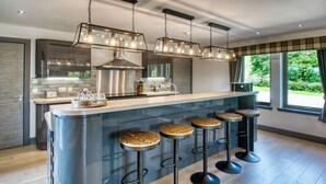Een moderne keuken met een centraal eiland, barstoelen, roestvrijstalen apparatuur en hangende lampen.