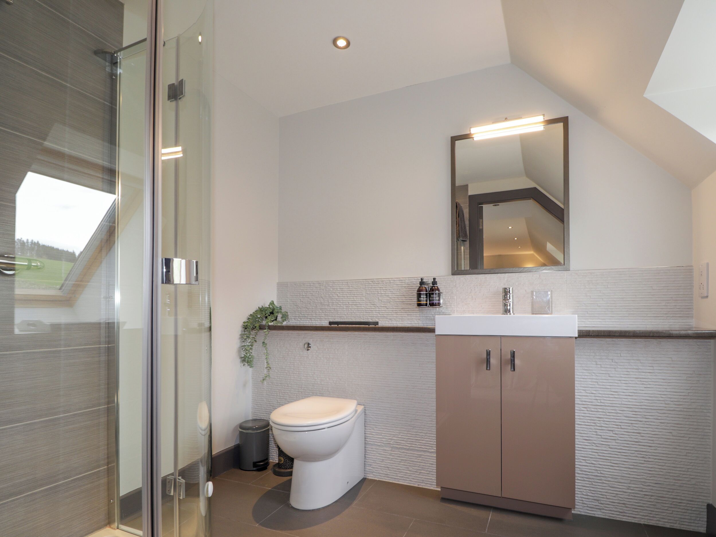 Une salle de bain moderne avec une douche à parois de verre, des toilettes blanches, un meuble beige et un miroir au-dessus du lavabo.