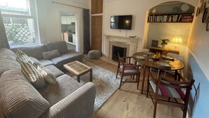 A living room with a sofa, coffee table, fireplace, TV, dining table, chairs, and a bookshelf. - Limpet Lodge (North Shields)