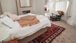 A bedroom with a large bed, a chair, a nightstand, a mirror, and a window with curtains. - Limpet Lodge (North Shields)
