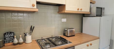 Una cocina con gabinetes color crema, estufa a gas, tostadora y microondas.