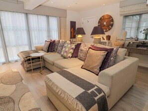 A modern living room with a sectional sofa, a small table, and a large wall clock. - Little Barn (Stockbridge)