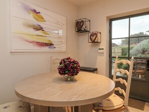 Un coin repas avec une table ronde, des chaises, un vase de fleurs, un tableau et une vue par la fenêtre.
