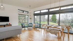Un salon spacieux doté d’un grand téléviseur, d’un plancher en bois et d’un coin repas avec une table dressée pour quatre personnes.