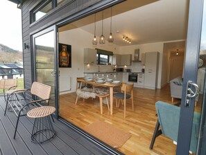 A modern kitchen with wooden cabinets, a dining area with a table set for four, and a view of the outdoors through large glass doors.