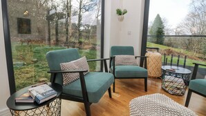 Un salon moderne avec deux fauteuils turquoise, une petite table ronde et une grande fenêtre donnant sur un jardin et des arbres.