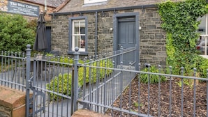 A stone cottage with a metal fence, a small porch, and a signboard. - Wee Cottage (Moffat)