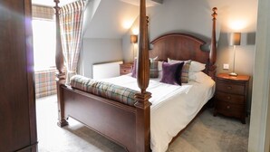 A four-poster bed with a wooden headboard, a bedside table with a lamp, and a window with curtains. - Wee Cottage (Moffat)