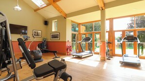 Ein Fitnessraum mit Trainingsgeräten, großen Fenstern und Holzbalken.