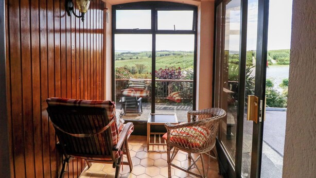 A room with a wooden ceiling and walls, a large window, and two wicker chairs. - An Radharc Álainn (Rosscarbery)