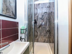 A bathroom with a glass-enclosed shower, a white bathtub, and a marble backsplash. - The Sail Loft (Y Felinheli)