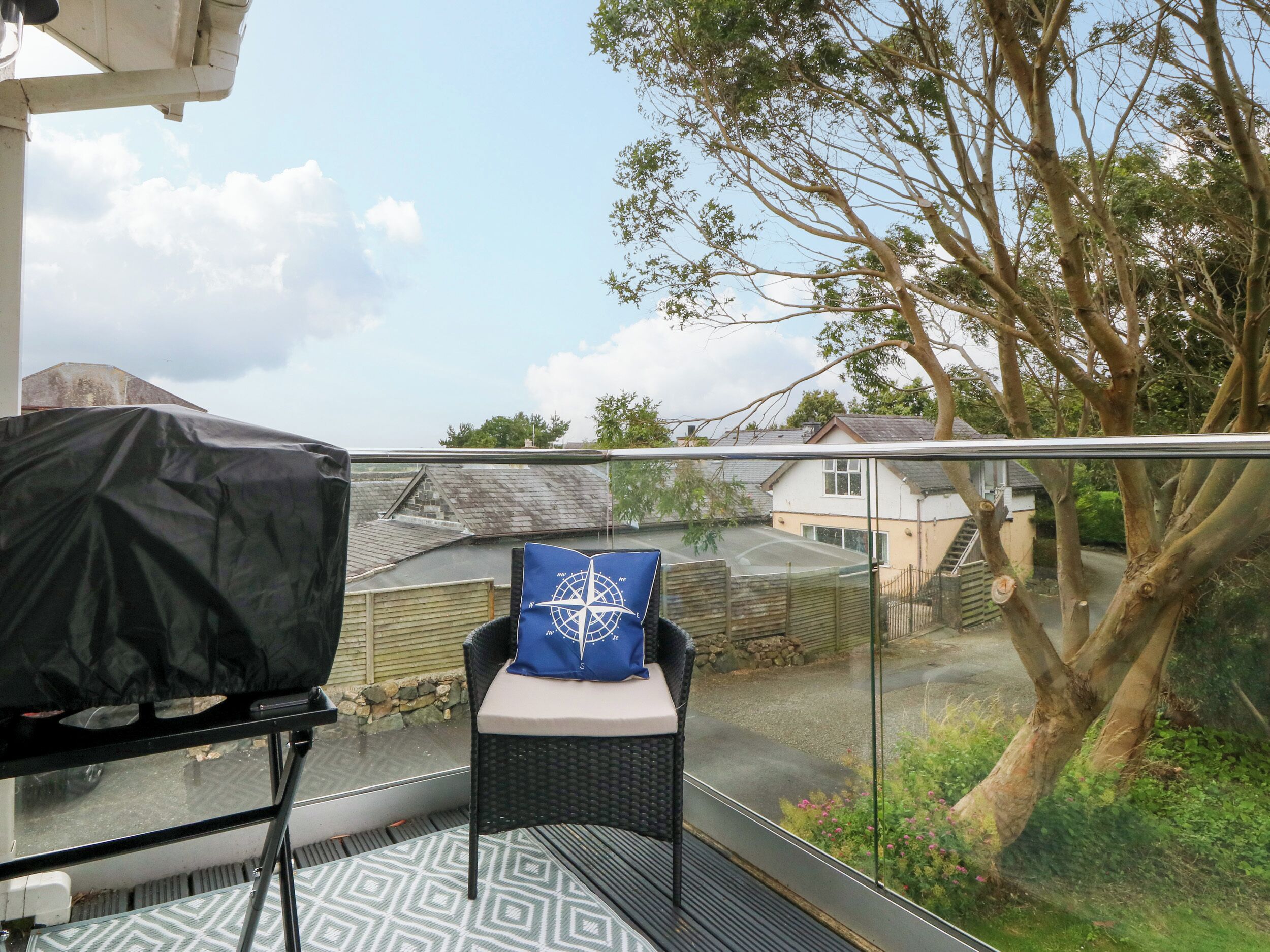 A balcony with a covered grill, a chair with a cushion, and a view of a residential area with houses and trees.