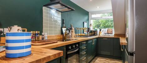 Een moderne keuken met een houten aanrecht, een grote blauw-witte container en een raam met uitzicht op groen.