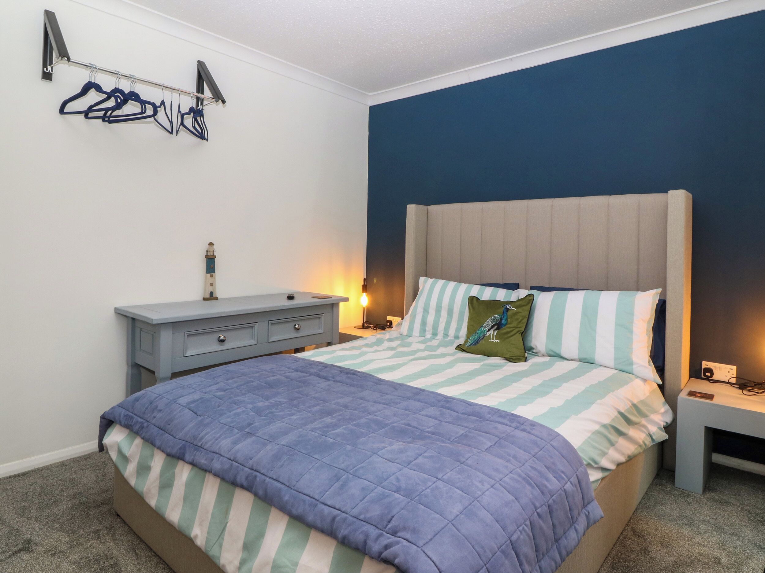 A bedroom with a bed, nightstands, a dresser, a lamp, and a coat rack with hangers.