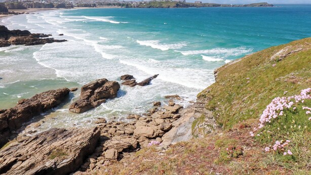 A coastal landscape with rocky shores, clear blue sea, and a distant town. - 119 Henver Road (Newquay)