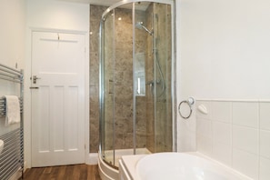 A modern bathroom with a glass-enclosed shower, a white bathtub, and a towel rack.