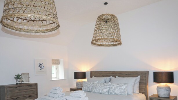 A bedroom with a wooden bed, two bedside tables with lamps, a bedside plant, and a window with a view. - Gwel-y-rhos (Llanfairpwllgwyngyll)
