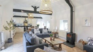 A spacious living area with a sofa set, a dining table, a fireplace, and a kitchen in the background. - Gwel-y-rhos (Llanfairpwllgwyngyll)
