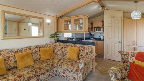Un'accogliente zona living con un divano floreale, mobili contenitori in legno e angolo cottura.