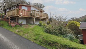 A two-story house with a wooden deck and a staircase leading to the upper floor. - Y Goedlan (Swansea)