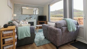 A living room with a fireplace, a television, and a view of a balcony with a wooden railing. - Y Goedlan (Swansea)