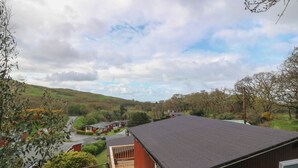 A residential property with a red building, a balcony, and a view of a green valley and hills. - Y Goedlan (Swansea)