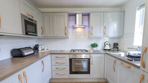 A modern kitchen with white cabinets, wooden handles, a built-in microwave, a gas stove, and a kettle. - Tranquil Waters (Windermere)