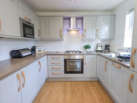 Una cocina moderna con armarios blancos, tiradores de madera, microondas integrado, cocina a gas y hervidor.