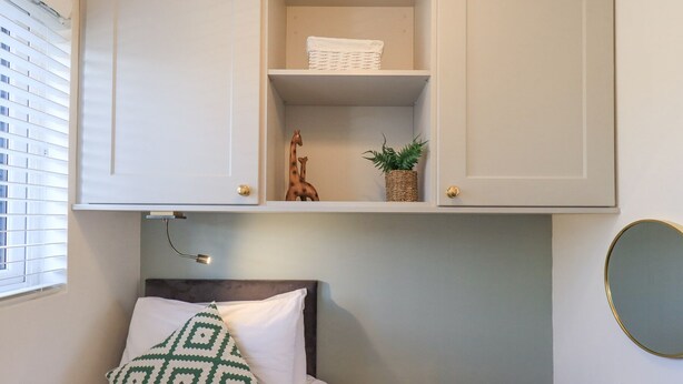 A bedroom with a bed, a bedside table, a lamp, a radiator, and a window with blinds. - Tranquil Waters (Windermere)