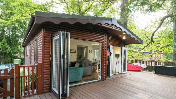 A wooden cabin with a sliding glass door leading to a living area with a sofa and a dining table. - Tranquil Waters (Windermere)