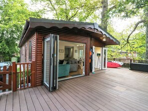 A wooden cabin with a sliding glass door leading to a living area with a sofa and a dining table. - Tranquil Waters (Windermere)