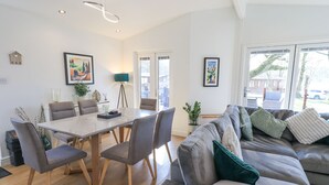 A modern living room with a dining area, featuring a sofa, chairs, a table, and artwork on the walls. - Tranquil Waters (Windermere)