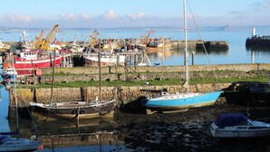 A harbor with various boats docked, including a red and white ship, a blue sailboat, and a black boat with a mast. - The Granary (Penzance)