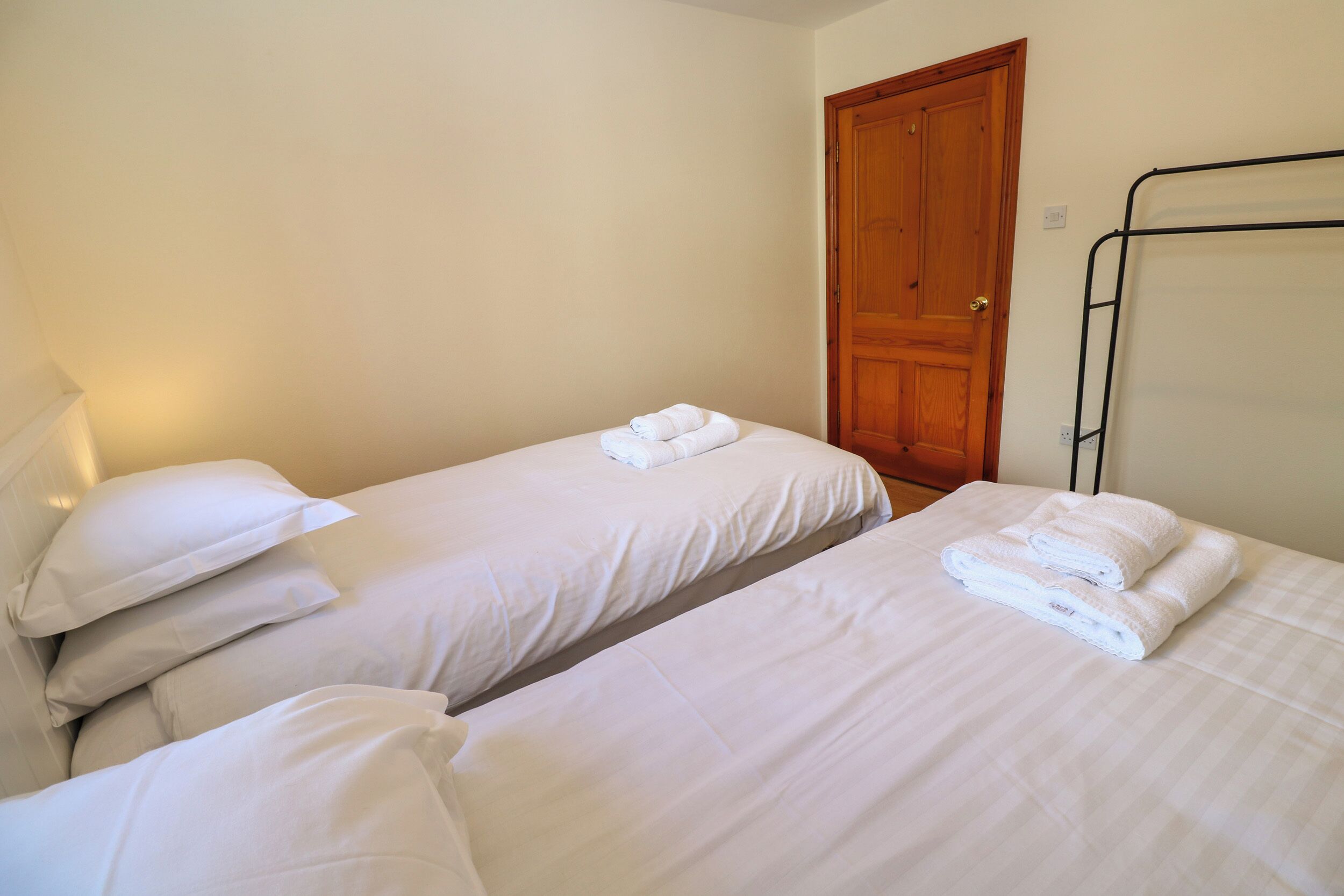 A room with two single beds, each with white linens and pillows, a wooden door, and a metal bed frame.