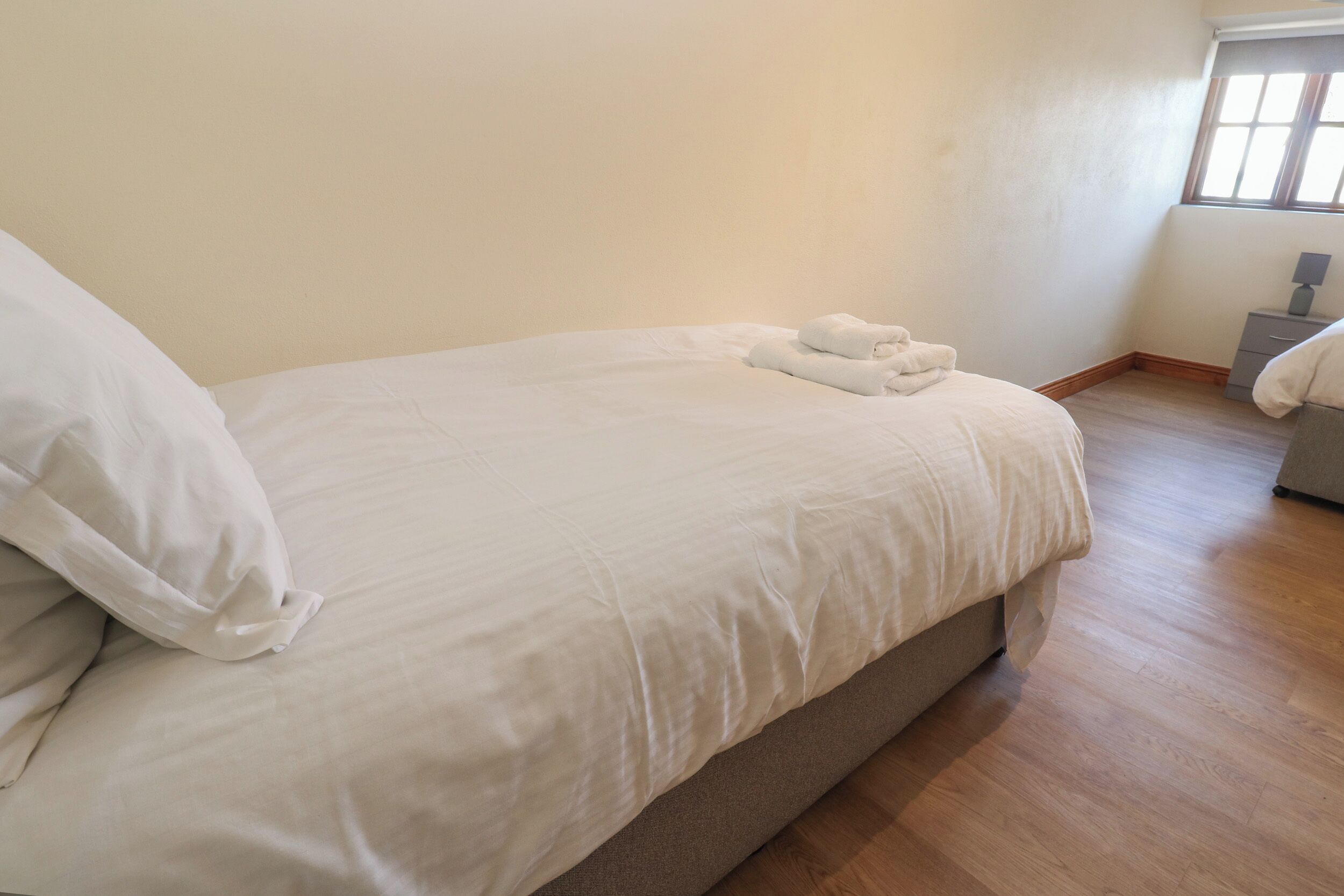 A neatly made bed with white linens and a folded towel on the side.