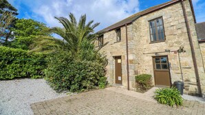 A stone building with a wooden door and windows, surrounded by greenery and a gravel path. - The Granary (Penzance)