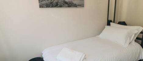 A neatly made bed with white linens, a black chair, and a framed black and white photograph on the wall.