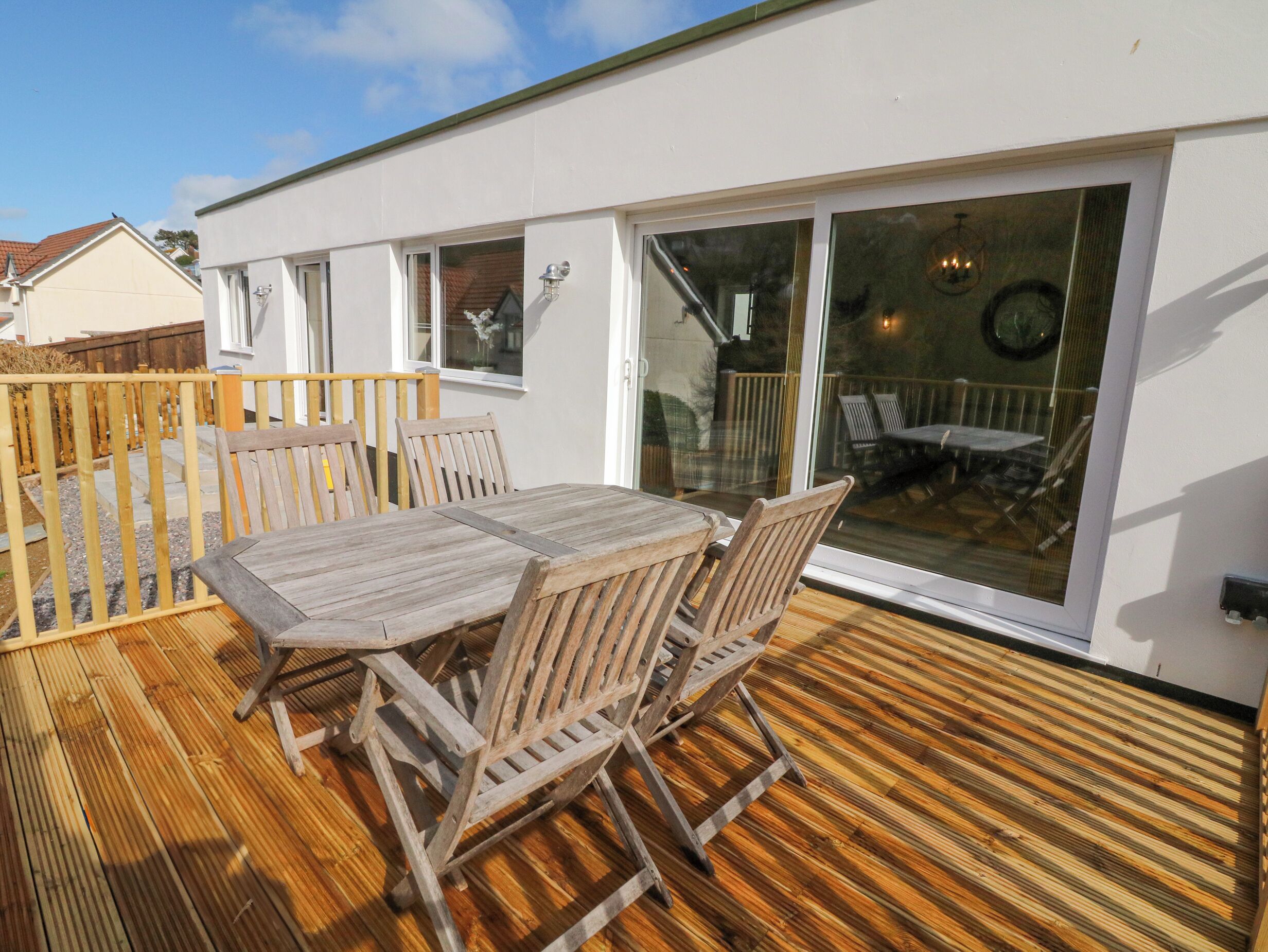 Une terrasse en bois avec une table et des chaises, de grandes portes-fenêtres coulissantes et une vue sur le jardin.