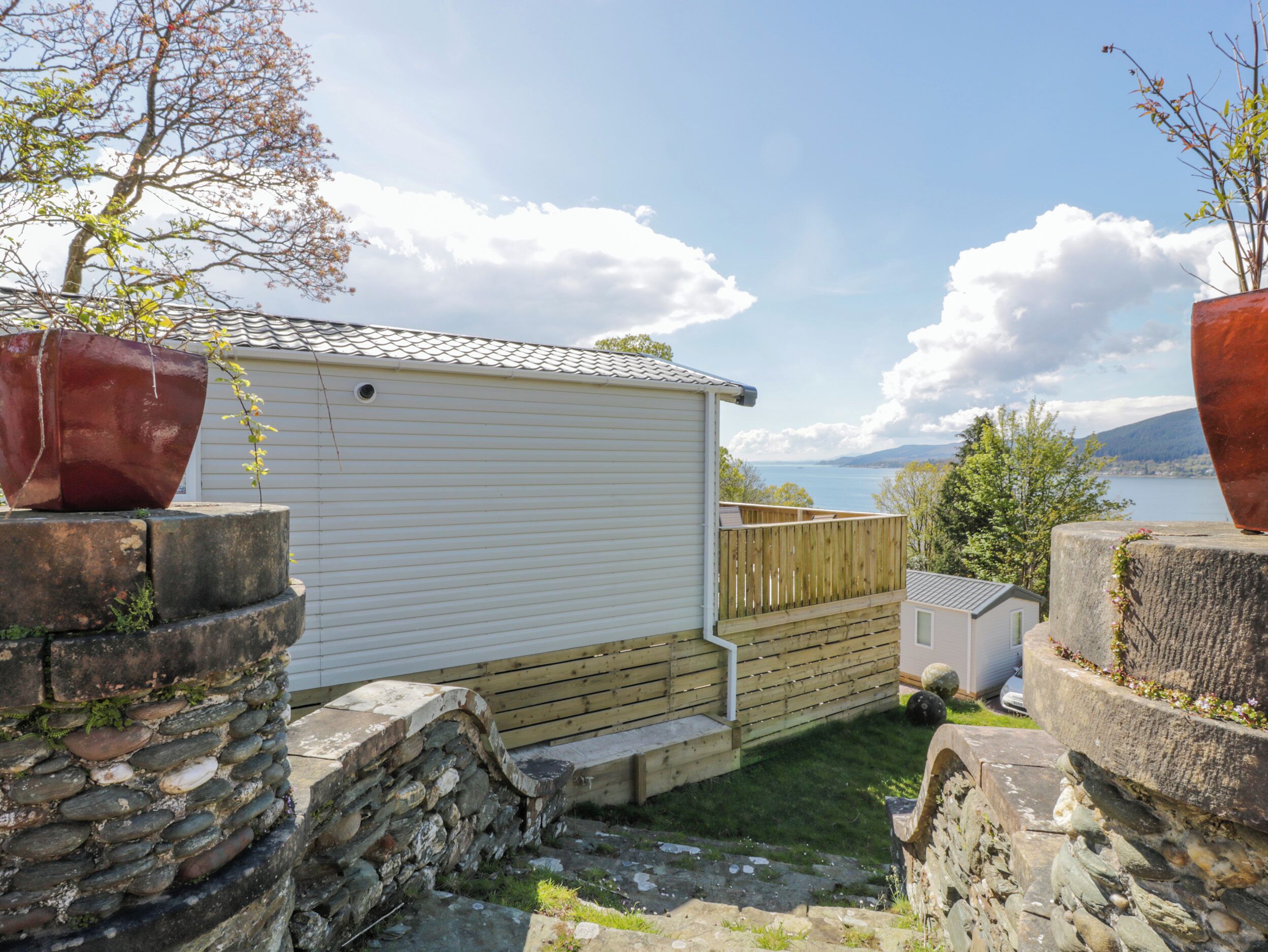 A white mobile home with a wooden deck and a stone wall.