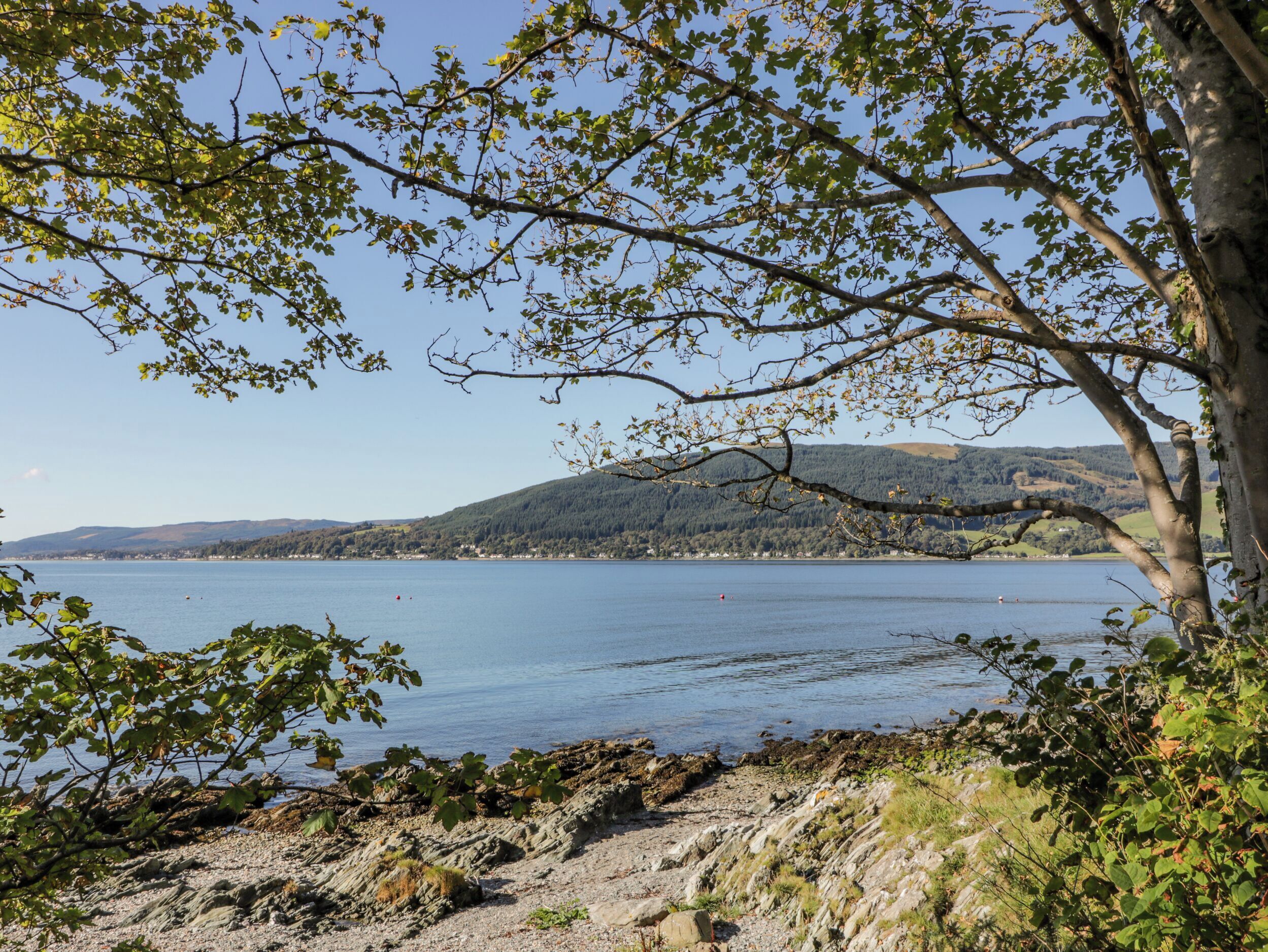 Eine Küstenlandschaft mit felsiger Küste, einem stillen See und Hügeln im Hintergrund.