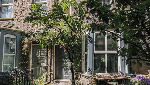 Een gebouw van steen met een tuininrichting, een houten bank en een metalen hek.