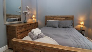 Een slaapkamer met een houten hoofdbord, een grote spiegel, twee bedlampen en een keurig opgemaakt bed met opgerolde handdoeken.