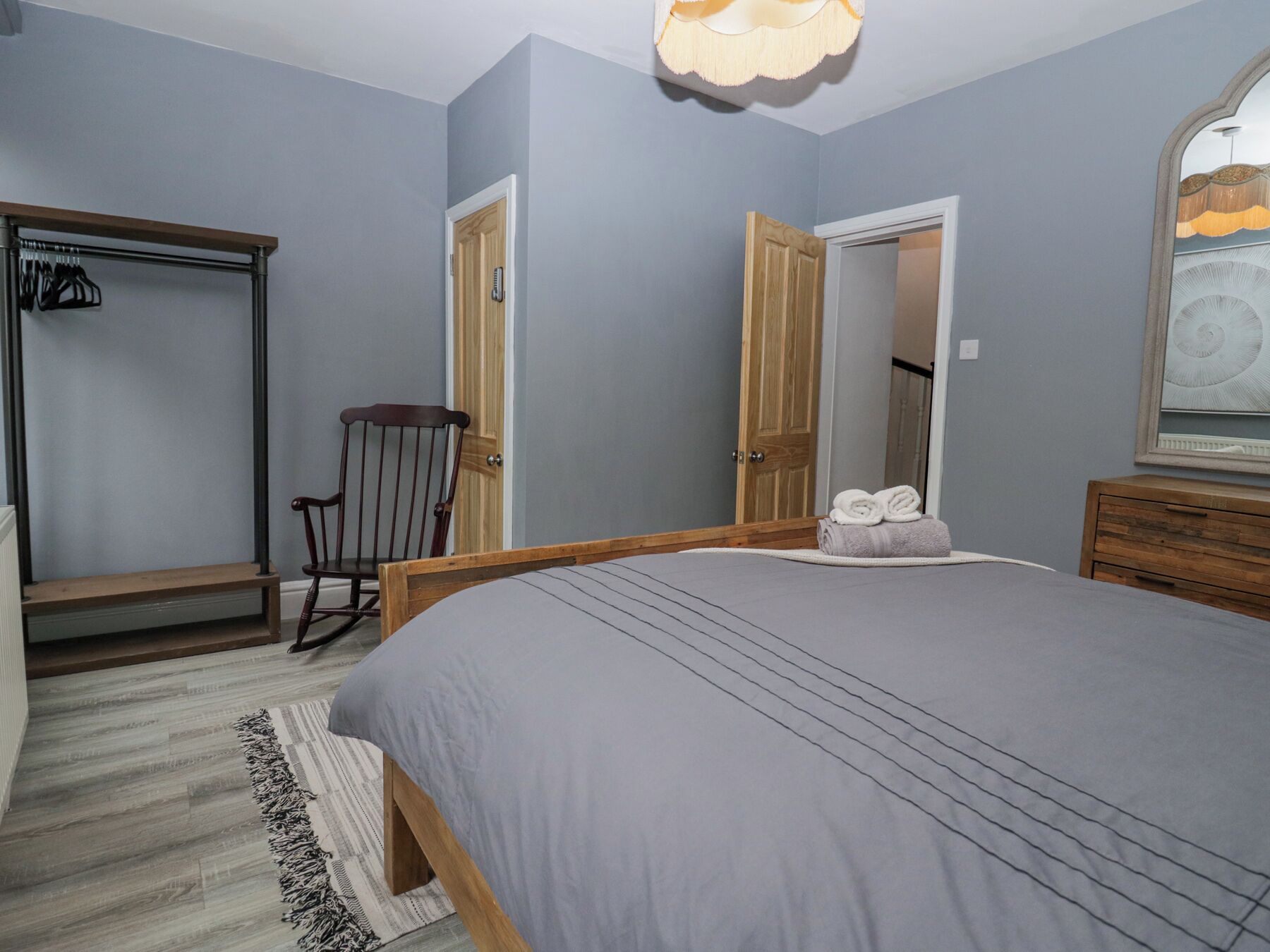 A bedroom with a bed, a wooden chair, a wardrobe, and a mirror on the wall.