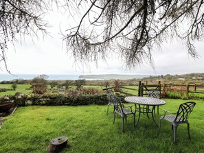 A grassy outdoor area with a metal table and chairs, a wooden fence, and a view of the countryside and sea. - Parc y Marriage (Newport)
