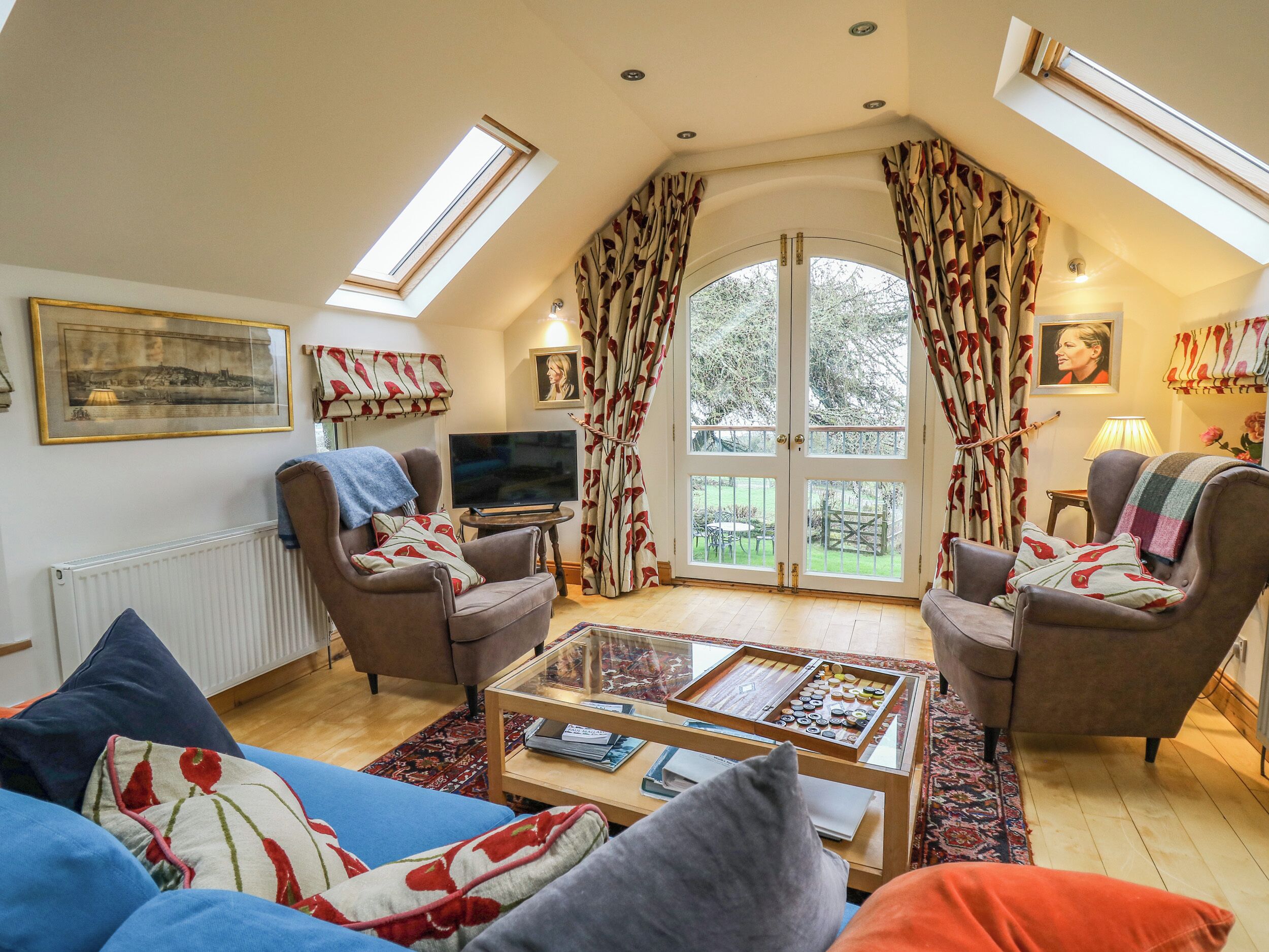 A cozy living room with a TV, comfortable seating, a coffee table, and a large window with curtains.