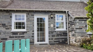 A stone house with a tiled roof, a white door, and a small porch area. - Ty Llaeth Cottage (Tywyn)
