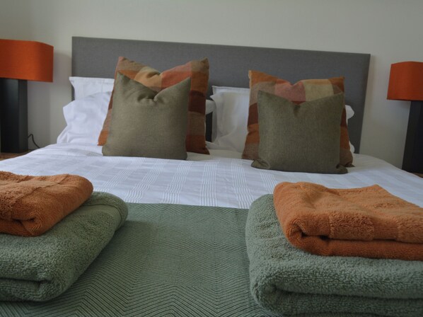 A neatly made bed with a grey headboard, two pillows, and two folded towels. - Taigh Marsaili (Harris)