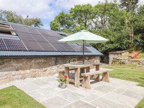 Un espace patio avec une table et des bancs en pierre, un pot de fleurs et un toit équipé de panneaux solaires.