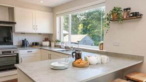 Een moderne keuken met een groot kookeiland, een inbouwoven en een raam met uitzicht op bomen.